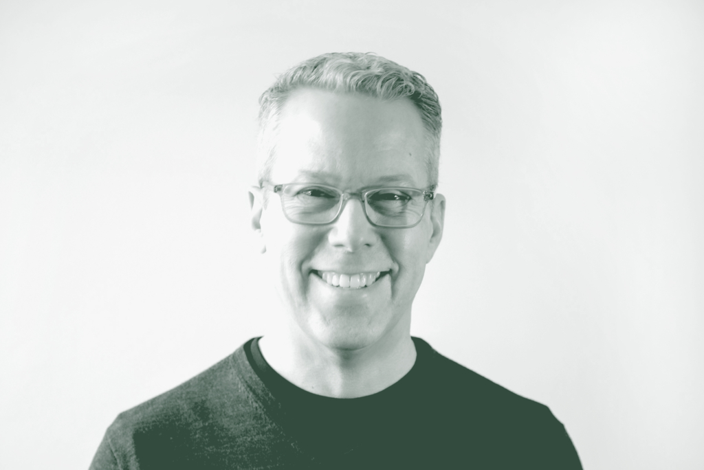 A black and white portrait of Russell Hagg, an Associate Principal and Senior Interior Design Leader with GFF in the Interior Design Studio, in front of a white background.