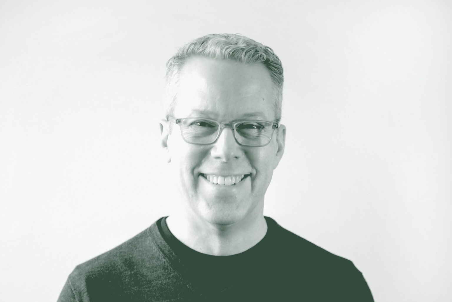 A black and white portrait of Russell Hagg, an Associate Principal and Senior Interior Design Leader with GFF in the Interior Design Studio, in front of a white background.