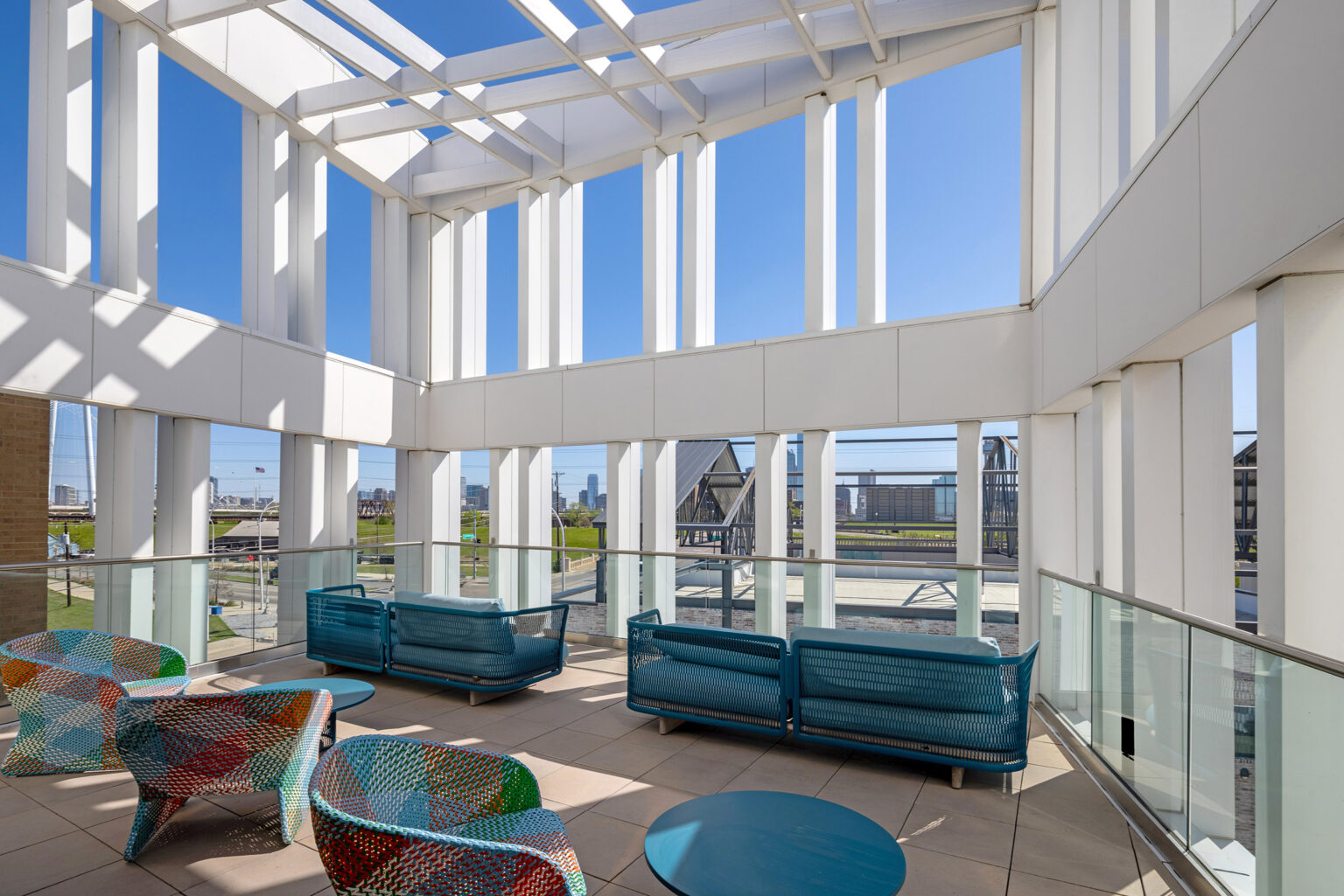 Top floor exterior deck of The Langford with colorful seating, white columns, and views of the Trinity River, Margaret Hunt Hill Bridge, and Downtown Dallas.