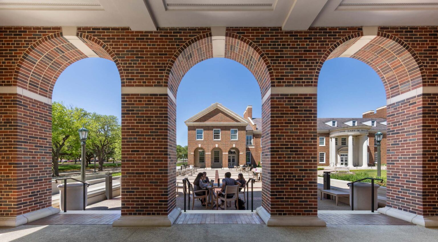 Brick arcade framing outdoor seating and pedestrian paths within the SMU Cox School of Business quadrangle.