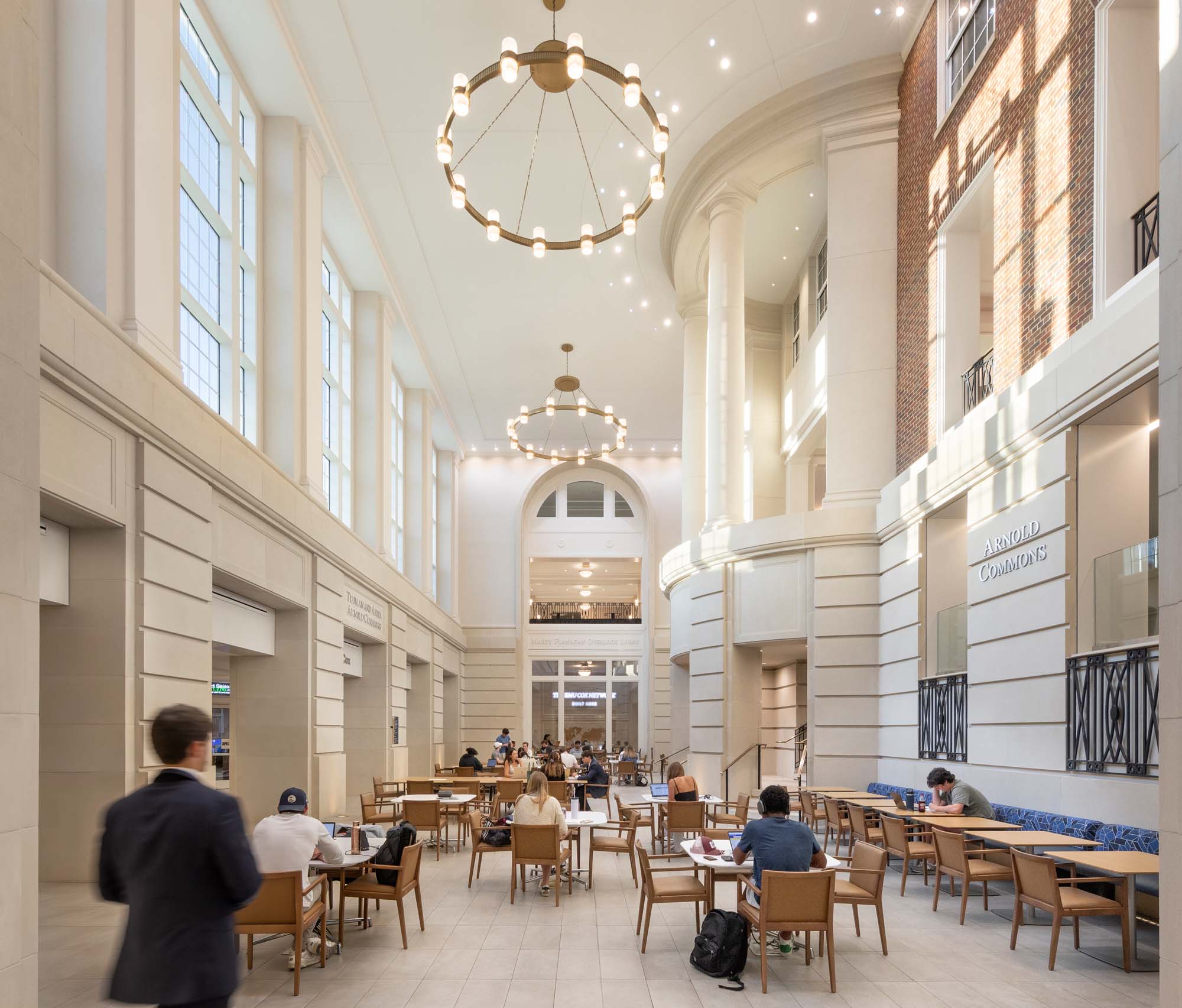 Multi-story interior commons with tall windows, classical columns, and communal seating at the SMU Cox School of Business.