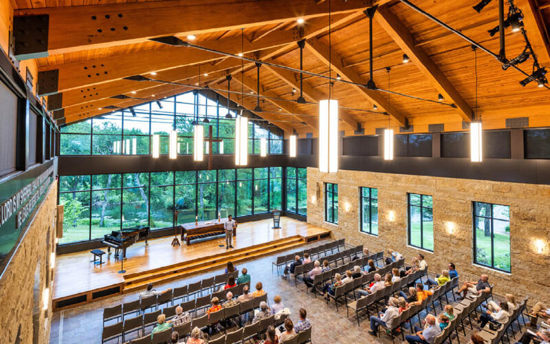 Interior of Hasley Chapel with warm wood beams, stone walls, and large windows framing views of the creek and pond.
