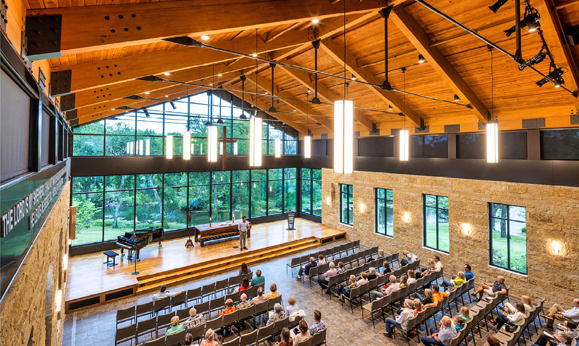 Interior of Hasley Chapel with warm wood beams, stone walls, and large windows framing views of the creek and pond.