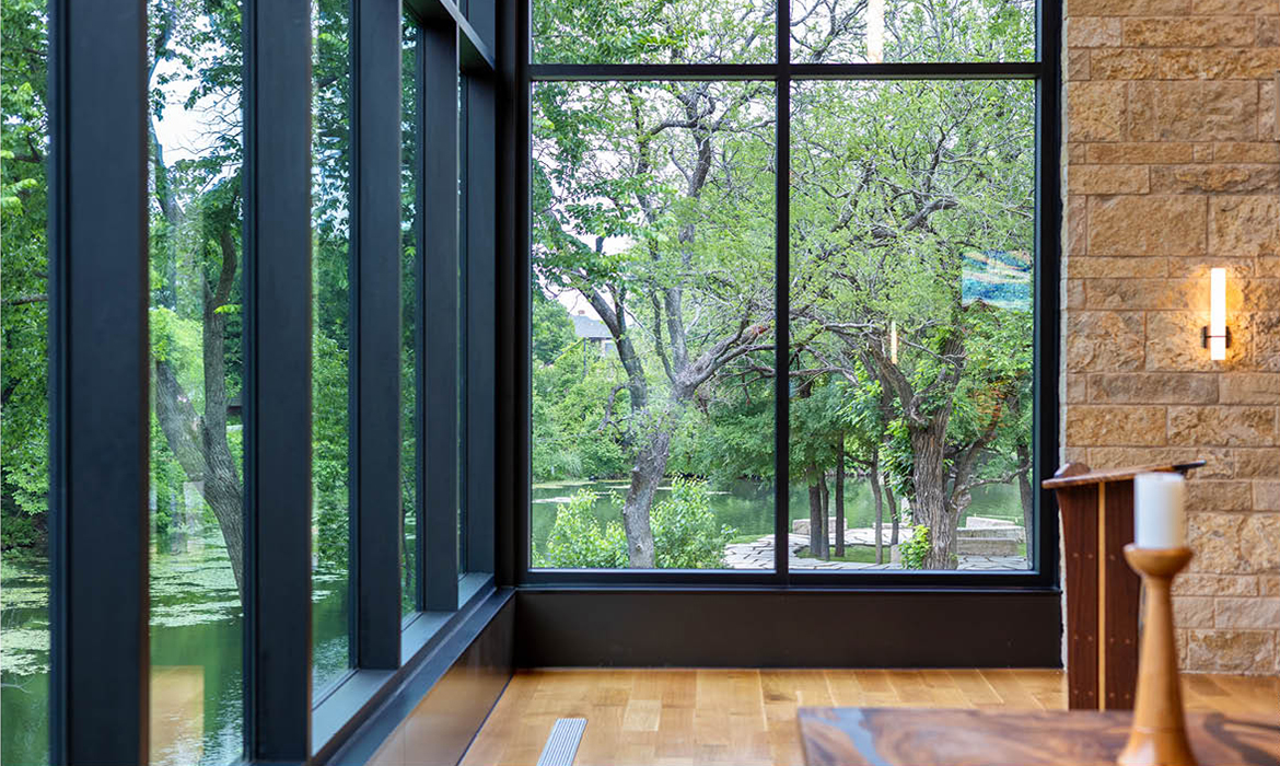 Close-up view of Hasley Chapel's corner window, framing lush greenery and a creek outside.