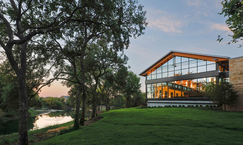 Exterior view of Hasley Chapel at sunset, featuring large glass windows reflecting the natural creek and trees.