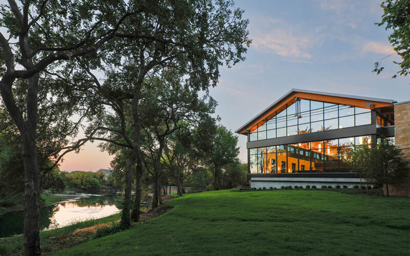 Exterior view of Hasley Chapel at sunset, featuring large glass windows reflecting the natural creek and trees.