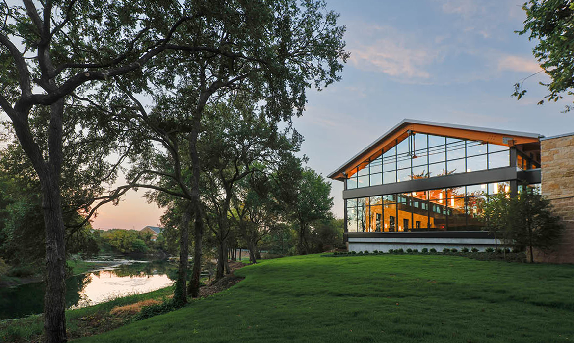 Exterior view of Hasley Chapel at sunset, featuring large glass windows reflecting the natural creek and trees.