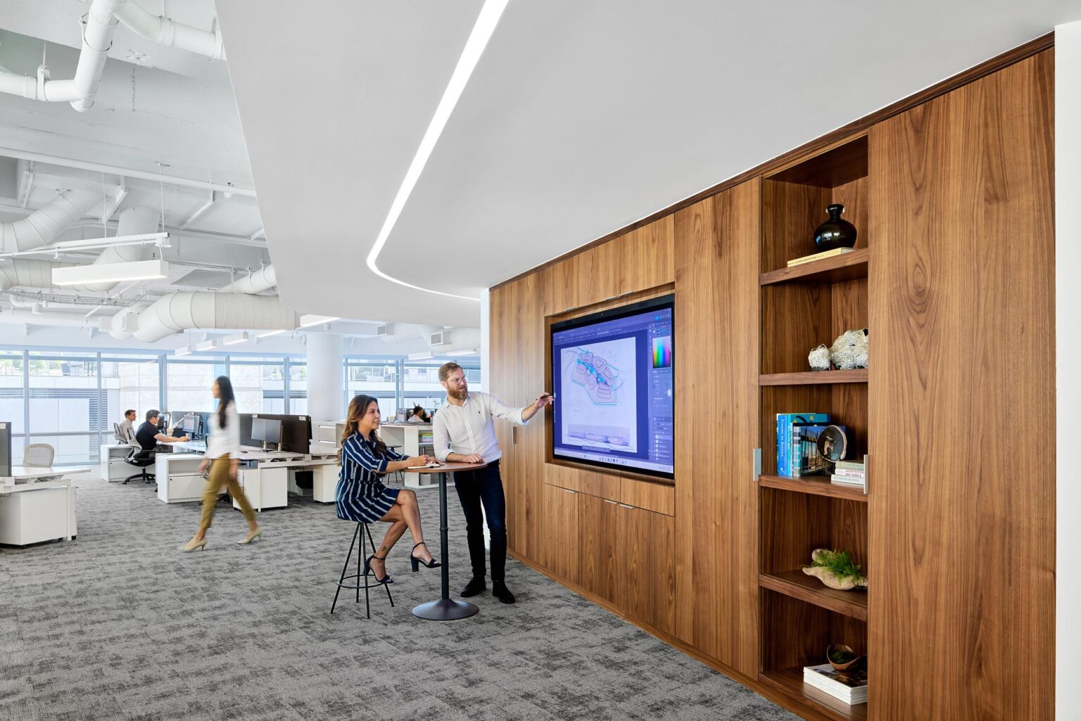 Open collaboration space with integrated walnut millwork, shelving, and digital display at GFF’s Dallas office, designed to support teamwork and flexible workplace strategy in a modern architecture environment.