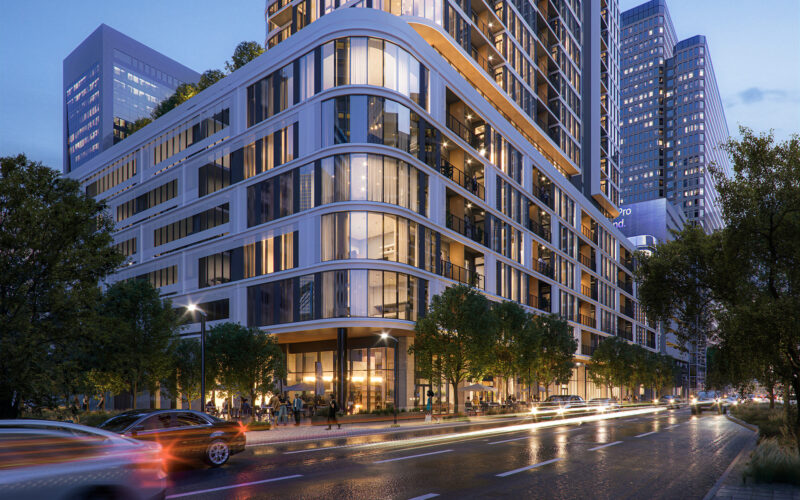 View of the curved corner façade of Empira 711 N Pearl at dusk, with illuminated windows and street lights reflecting off the building's glass and metal surfaces.