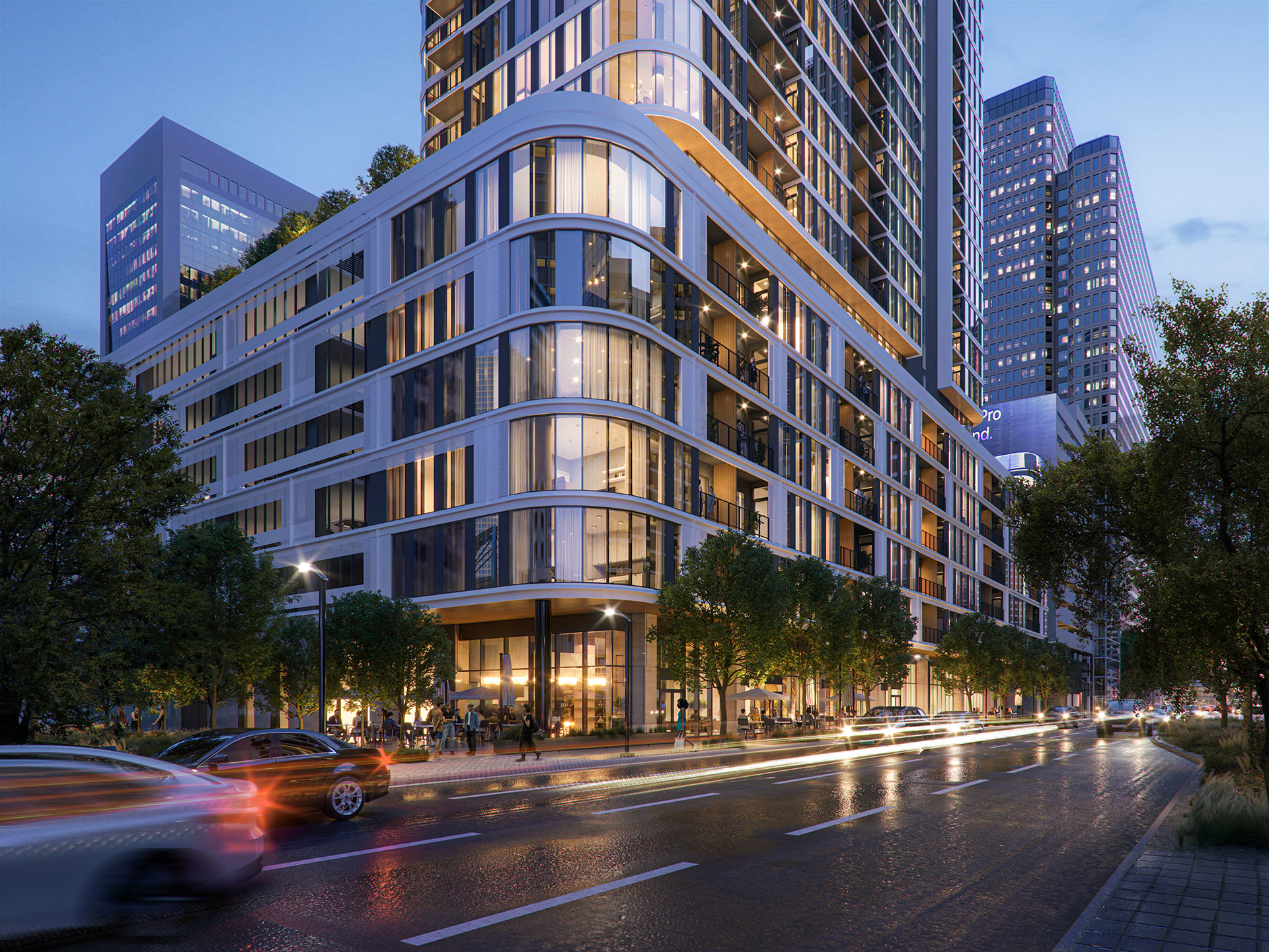 View of the curved corner façade of Empira 711 N Pearl at dusk, with illuminated windows and street lights reflecting off the building's glass and metal surfaces.