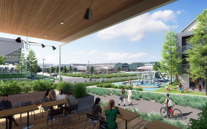 Perspective rendering from a covered patio at Assembly Park, showing outdoor dining tables overlooking a landscaped plaza with walking paths, planted seating areas, and a children's play zone. In the background, retail storefronts and a stage structure provide an active gathering space.