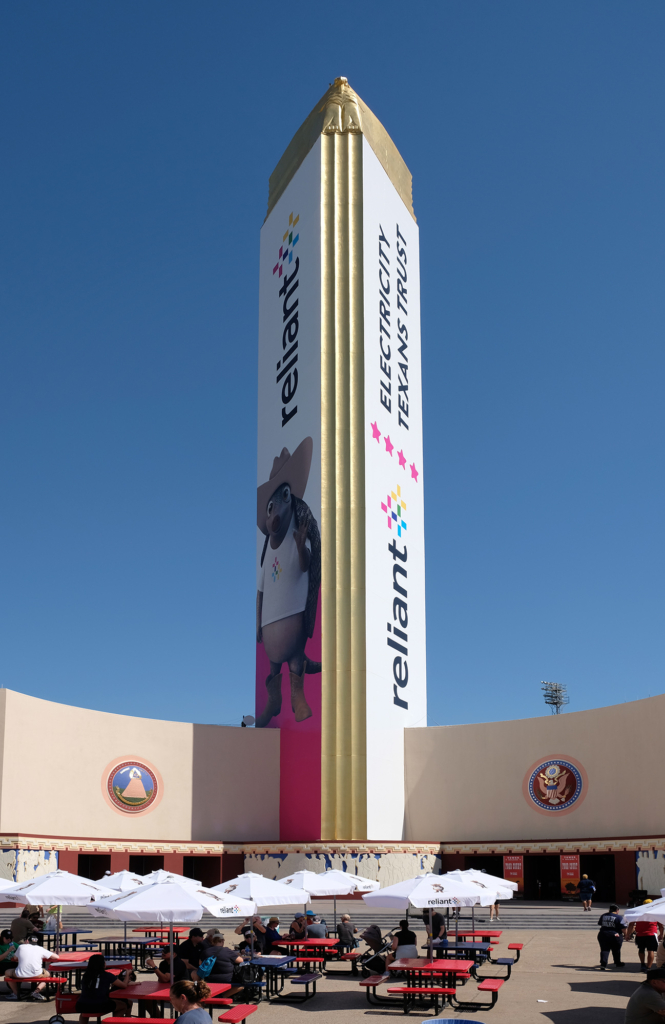 Fair Park Tower Building with its gold-clad spire and surrounding seating plaza on a sunny day.
