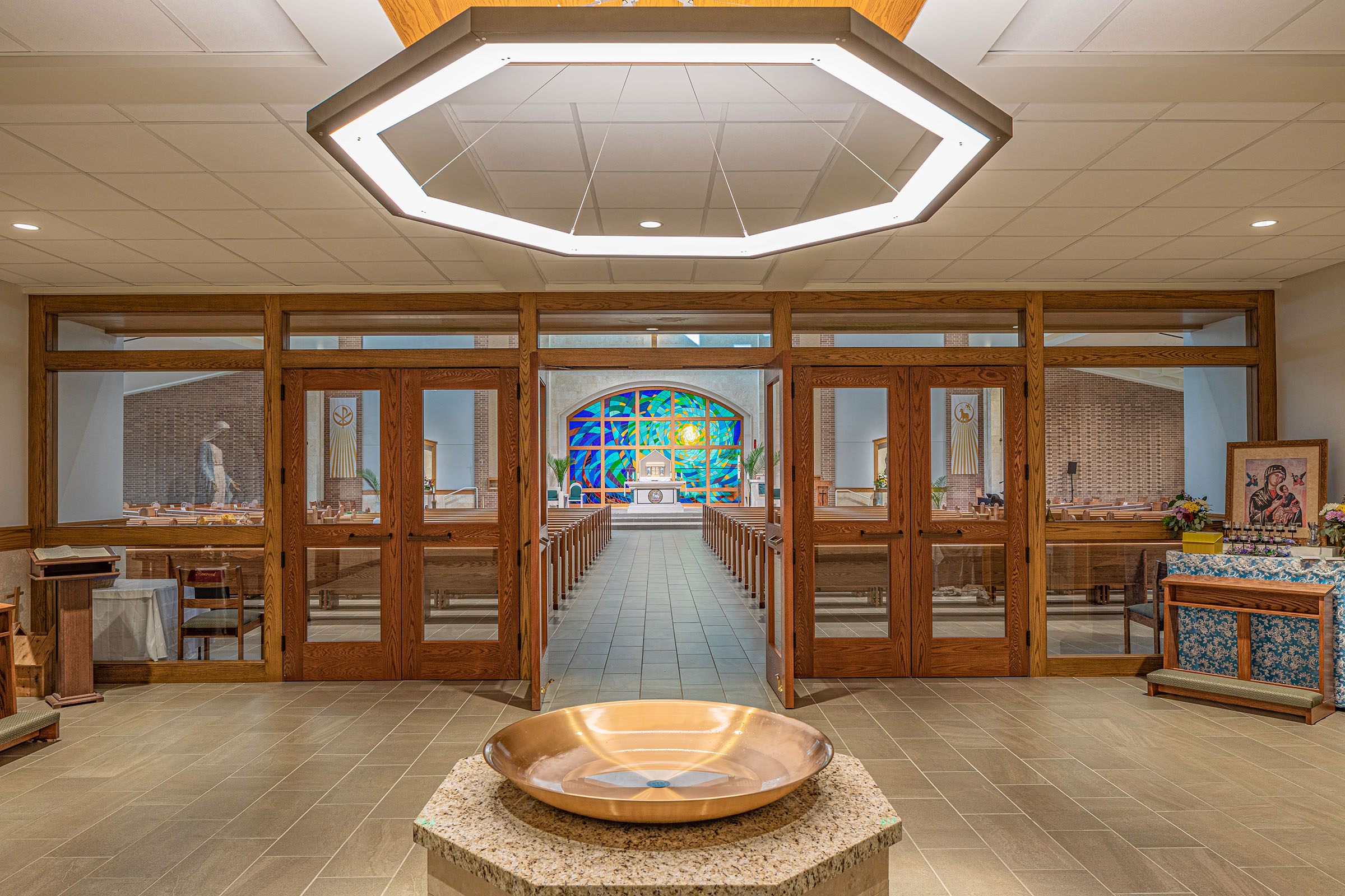 Narthex Interior view of the narthex with stained wood-framed doors, a central baptistry, and a glimpse of the nave beyond.