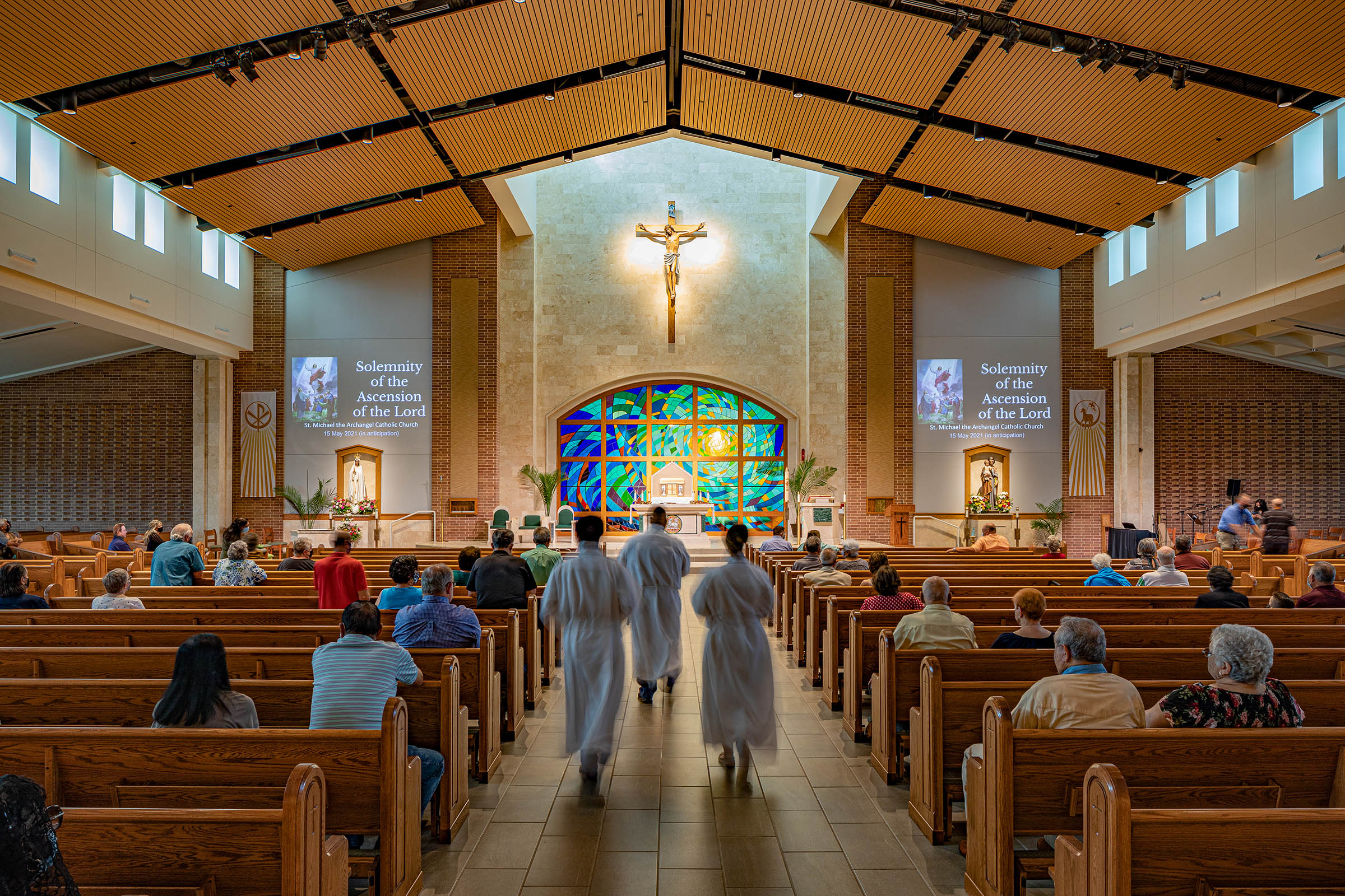 Nave Rear view of the nave showcasing fan-shaped seating, stained glass at the altar, and a warm wood ceiling.