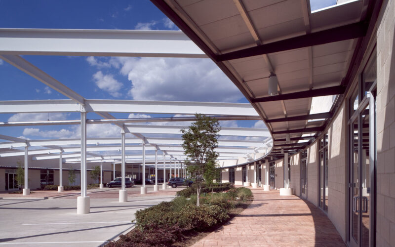Interior courtyard with steel roof skeleton providing shade, surrounded by showroom entrances and landscaped pathways.