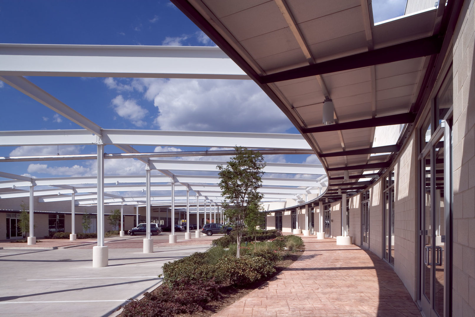 Interior courtyard with steel roof skeleton providing shade, surrounded by showroom entrances and landscaped pathways.