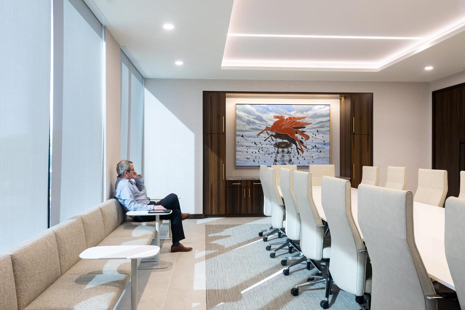 Wide view of a boardroom featuring tall chairs, a long white table, dark wood walls, and banquette seating.