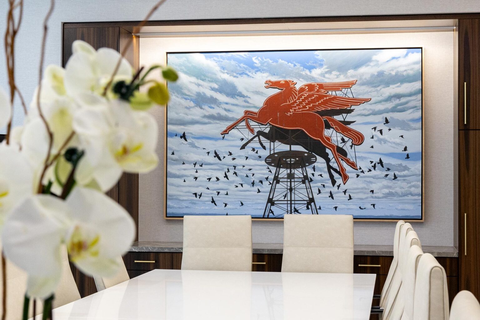 Orchid flowers in foreground with a large Pegasus artwork and boardroom chairs in background.