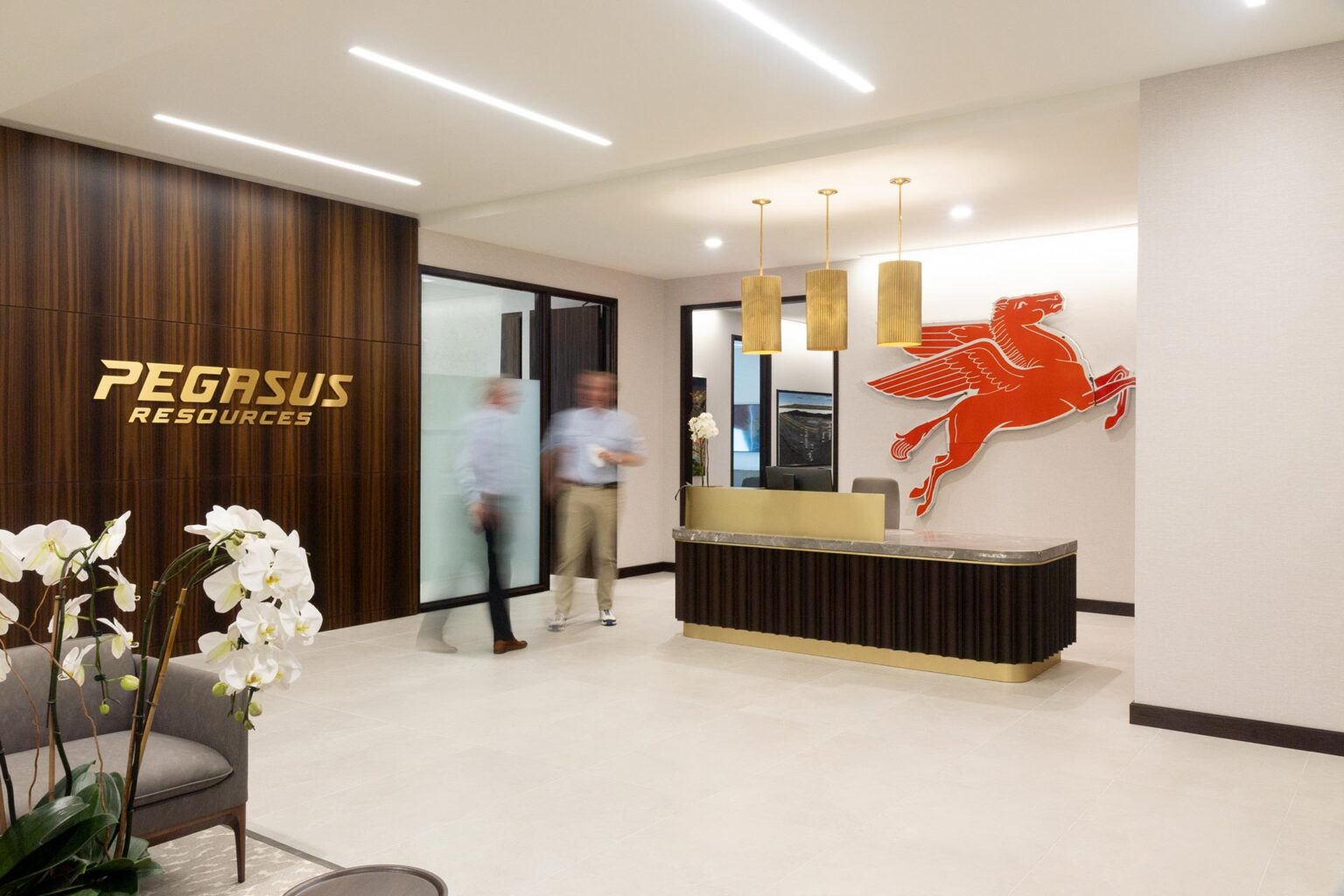 Reception desk in a light-tiled lobby with overhead lighting and a red Pegasus wall emblem.