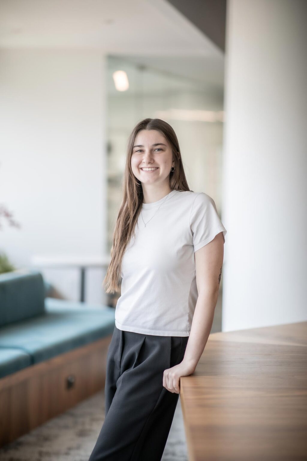 Allison Brooks, Architectural Intern at GFF, standing in a bright office near a wood table wearing a white shirt and black pants.