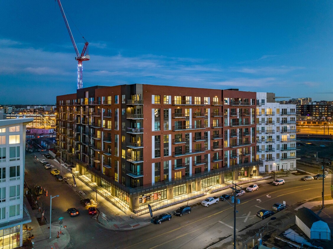 Exterior street-level perspective of Denargo Market Phase 3 mixed-use mid-rise with brick and white panel façade, retail storefronts, and residential balconies in Denver’s RiNo district.
