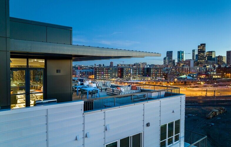 Rooftop terrace of Denargo Market Phase 3 featuring lounge seating and open views of downtown Denver skyline and Rockies Stadium at twilight.