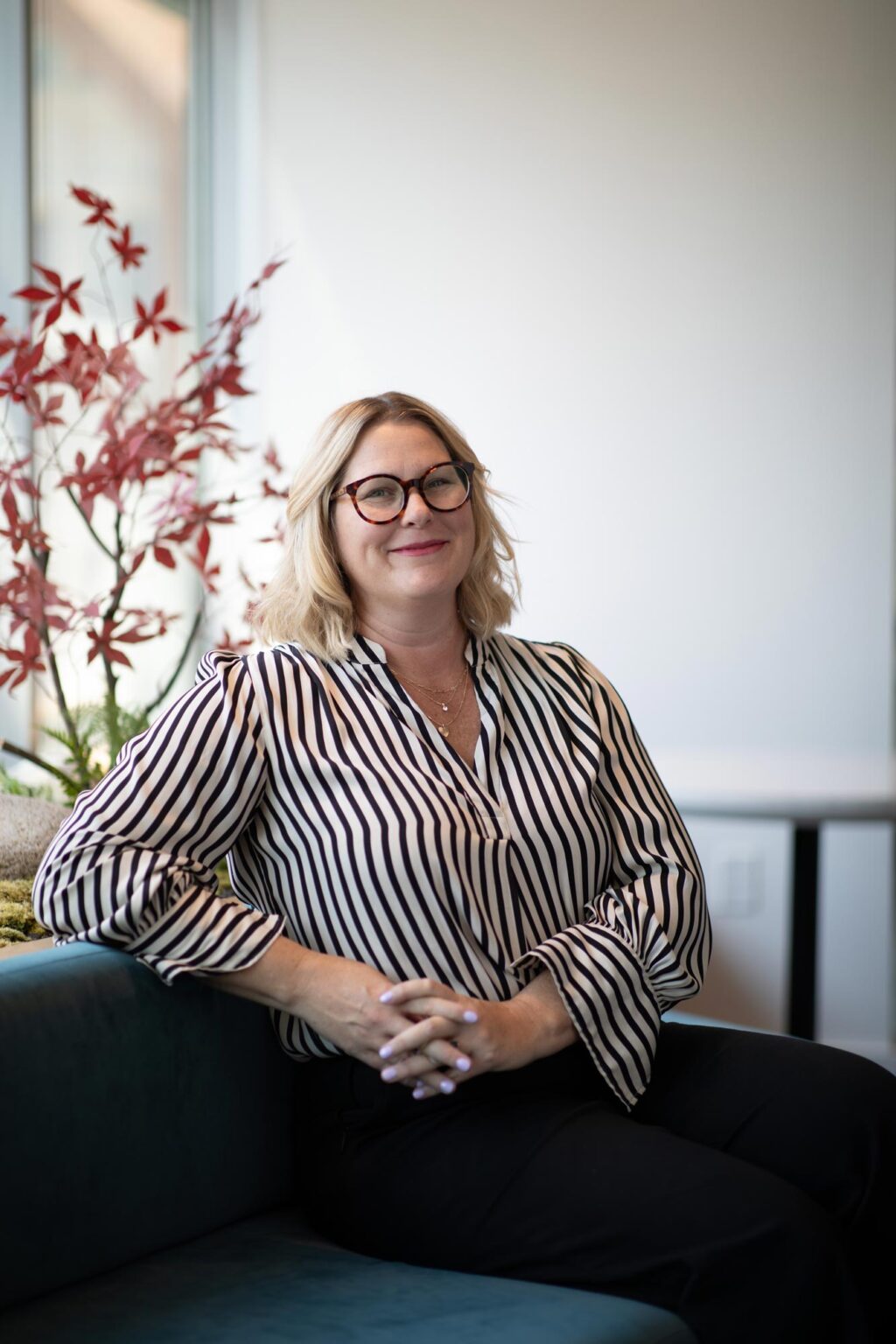Erin Nies, Associate and Senior Project Leader at GFF, seated in the Austin office with striped blouse and glasses, photographed in a modern design studio environment.