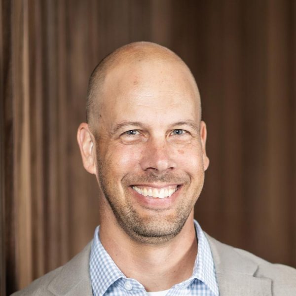 Aaron Hunt, AIA, Managing Director of GFF Fort Worth and Denver, close-up professional portrait with a wood-paneled office wall backdrop.
