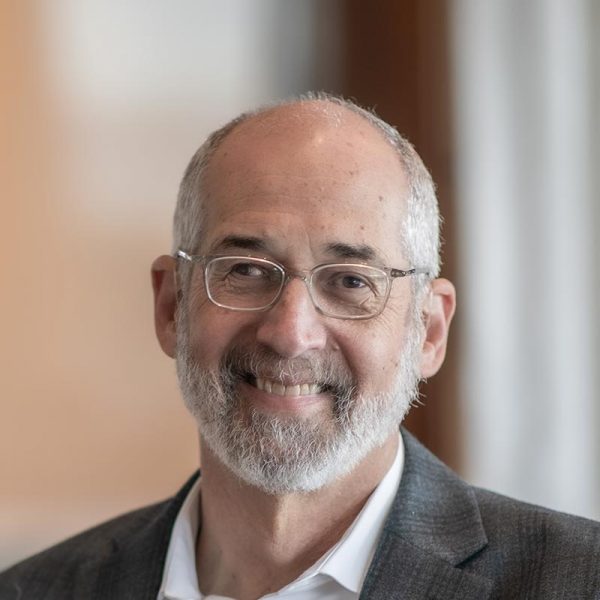 Jon Rollins, Principal at GFF, close-up portrait with glasses, beard, and suit jacket, photographed in a modern office background.