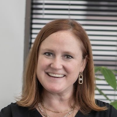 Sara Good, Associate and Studio Director at GFF, close-up portrait with window blinds and plant in background, wearing gold jewelry and black blouse.