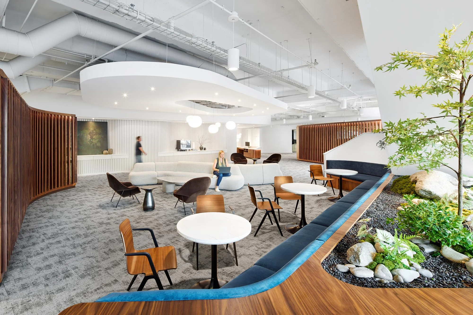 Shared work lounge at GFF’s Dallas headquarters with curved wood seating, integrated greenery, and a biophilic design approach combining open office strategy with hospitality-inspired interior architecture.